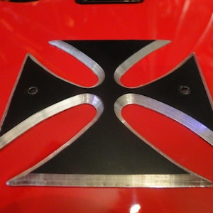 Puede incluir: Una cruz de metal negro con un borde plateado, montada sobre una superficie roja.