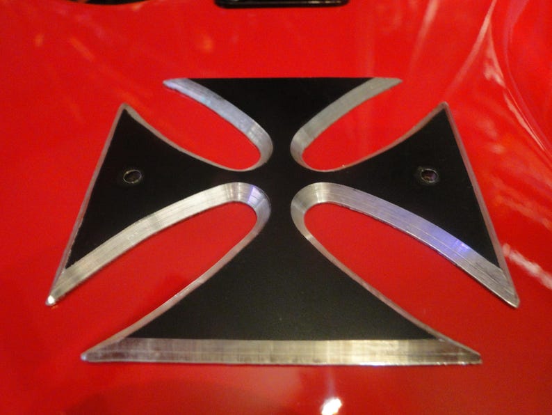 Puede incluir: Una cruz de metal negro con un borde plateado, montada sobre una superficie roja.