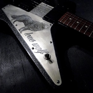 Könnte beinhalten: Eine schwarze E-Gitarre mit einem silbernen Metall-Pickguard, auf dem ein Wolf und der Text "lone wolf" eingraviert sind.