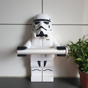 Könnte beinhalten: Weißer Toilettenpapierhalter aus Kunststoff in Form einer LEGO-Figur von Star Wars Stormtrooper. Die Figur hält eine Rolle Toilettenpapier.