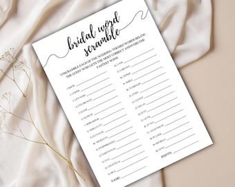 May include: A white paper with the text "bridal word scramble" in a handwritten font. The game sheet has lines for unscrambled words and a space for the guest's name and points. The paper is on a beige surface.