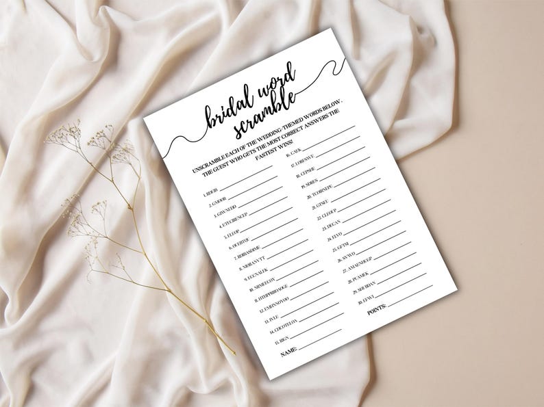 Op de afbeelding: Een wit papier met de tekst "bridal word scramble" in een handgeschreven lettertype. Het spelblad heeft lijnen voor ontsleutelde woorden en een ruimte voor de naam en punten van de gast. Het papier ligt op een beige oppervlak.