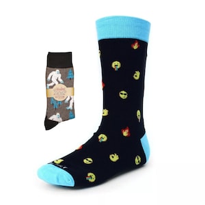 May include: A pair of black socks with a blue cuff. The socks feature a pattern of yellow smiley faces with different expressions, including a tongue sticking out, sunglasses, and a fire emoji. The socks are shown with a pair of gray socks with a white yeti and pine tree pattern.
