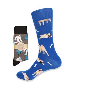 May include: A pair of blue socks with a pattern of pugs and bones. The socks are shown with a pair of gray socks with a pattern of a yeti and trees. The gray socks have a tag that says "Happy Yeti" with a small snowman graphic.