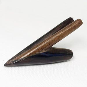 Könnte beinhalten: Handgefertigtes Holzobjekt mit dunkelbraunem Sockel und zwei hellbraunen, abgewinkelten Stäben. Das Objekt hat eine glatte, polierte Oberfläche und ein einzigartiges, abstraktes Design. Die Holzmaserung ist sichtbar und trägt zu seiner natürlichen Ästhetik bei.