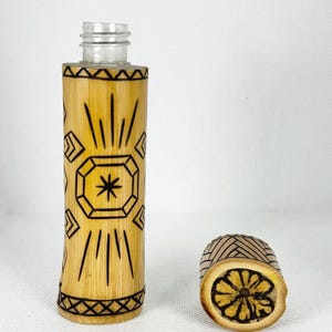 Peut inclure: Une petite bouteille en verre transparente avec un couvercle et une base en bambou. Le bambou est décoré d'un motif géométrique noir.