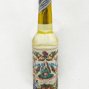 May include: A bottle of Agua de Florida, a floral-scented cologne. The bottle has a gold foil top and a label with floral and scroll designs. The text "Agua de Florida" and "Murray & Lanman" are visible.