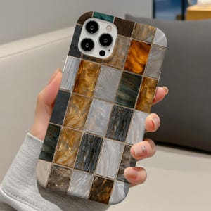 Puede incluir: Una funda de teléfono inteligente con un diseño de mosaico. La funda presenta un patrón de cuadrícula de baldosas rectangulares en tonos marrón, dorado, gris y verde. La funda tiene un acabado brillante y un recorte para la cámara.