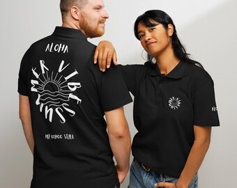 Op de afbeelding: Twee zwarte poloshirts met witte tekst en grafische ontwerpen. Een shirt zegt "Aloha Mer Vibes Sun My Soho Style" en de andere heeft een zon- en golfmotief.
