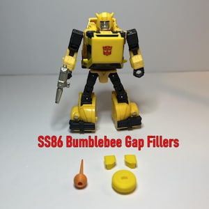 Peut inclure: Une figurine articulée Bumblebee jaune et noire avec un pistolet argenté. La figurine porte un emblème rouge sur la poitrine. L'image montre également plusieurs accessoires jaunes et orange, et le texte "SS86 Bumblebee Gap Fillers".