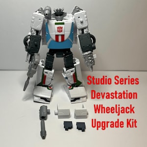May include: A white and blue action figure with black and gray accents, featuring a red and white emblem on its chest. The figure is accompanied by several gray and black upgrade kit pieces. Text on the image reads "Studio Series Devastation Wheeljack Upgrade Kit."