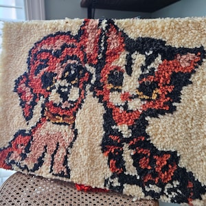 以下が含まれることがあります： 猫と犬のデザインのヴィンテージなラグフック。猫は黒とオレンジ、犬はオレンジと白。ラグはクリーム色で、毛足の長い質感です。