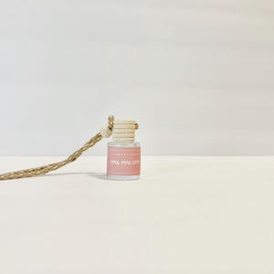 May include: A pink car air freshener with a string hanging from the top. The bottle is clear and has a label that says "Pink Pineapple".