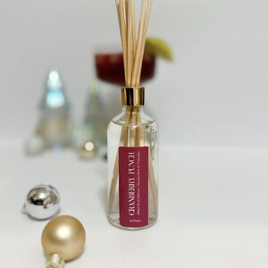 May include: A clear glass bottle with a gold cap and reeds, labeled "CRANBERRY PUNCH". The bottle is filled with a clear liquid. Decorative gold and silver ornaments are in the foreground, with a blurred cocktail in the background.