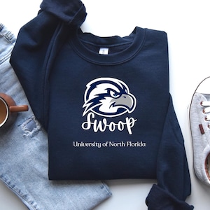May include: A navy blue sweatshirt with a white graphic of a falcon head with the text "SWOOP University of North Florida".