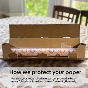 May include: A roll of patterned wrapping paper inside a cardboard box. The paper features a repeating design of teapots and teacups in pink, purple, and gold on a cream background. The box is open, showing the paper ready for shipping.