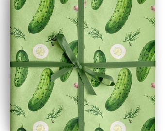 May include: Gift wrap featuring a repeating pattern of green pickles, dill sprigs, and lemon slices on a light green background. A dark green ribbon is tied around the package in a bow.