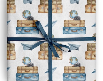 May include: A white gift wrap paper featuring a repeating watercolor pattern of stacked tan and blue suitcases, globes, cameras, and paper airplanes, tied with a dark blue satin ribbon centered across the middle of the package.