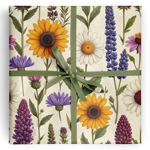 May include: Square gift wrap featuring a botanical design with sunflowers, daisies, and purple and blue wildflowers on a cream background. The gift is tied with a green ribbon in a bow.