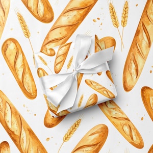 May include: White gift wrap featuring a watercolor pattern of golden baguettes and wheat stalks. A wrapped gift with a white satin ribbon is in the center. The design has a bakery theme.