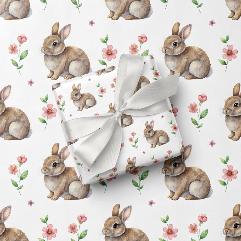 May include: White gift wrap featuring a repeating pattern of brown bunnies and pink flowers. A wrapped gift with a white satin bow is in the foreground. The overall design is a charming, spring-themed pattern.