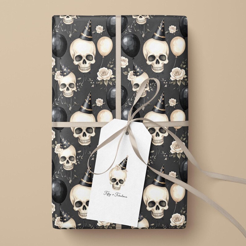 May include: Wrapped gift with a black and white skull pattern, party hats, balloons, and roses. A white tag with a skull illustration and the text "Fifty + Fabulous" is attached with a gray ribbon. The wrapping paper has a dark background.