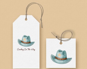 May include: Two white gift tags with watercolor illustrations of a cowboy hat. The hat is light blue with a brown band and a yellow star. One tag has the text "Cowboy On The Way". The tags are connected with a brown string.