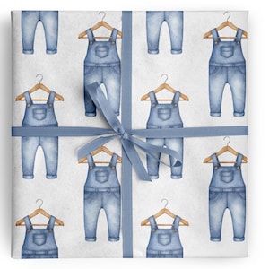 May include: Gift wrap featuring a repeating pattern of watercolor denim overalls on wooden hangers. The overalls are light blue, and the background is white. A blue ribbon is tied around the package.