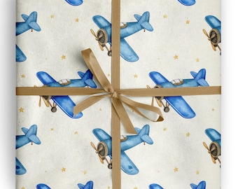 May include: Wrapping paper featuring a repeating watercolor pattern of blue propeller airplanes and small yellow stars on a light beige background, secured with a smooth, light brown ribbon tied in a centered cross pattern.