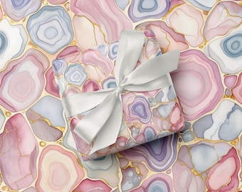 May include: A gift wrapped in paper with a watercolor agate stone pattern in shades of pink, purple, and gray, accented with gold veins. The gift is tied with a white satin ribbon, creating a soft and elegant presentation.