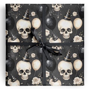 May include: Gift wrap featuring a repeating pattern of skulls wearing party hats, black balloons, and cream-colored roses on a dark background. The gift is tied with a black ribbon and bow.