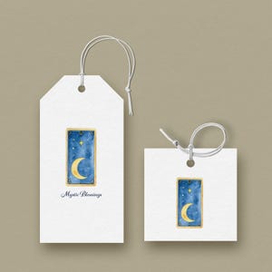 Könnte beinhalten: Zwei weiße Geschenkanhänger mit Schnur, einer rechteckig und einer quadratisch. Jeder Anhänger zeigt ein Aquarelldesign eines Mondes und Sterne auf blauem Hintergrund, goldfarben umrahmt. Der rechteckige Anhänger hat den Text "Mystic Blessings".