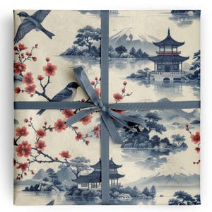 May include: Gift-wrapped package featuring a Japanese-inspired design. The wrapping paper showcases a serene landscape with pagodas, mountains, and cherry blossoms in shades of blue and red. A gray ribbon is tied around the package.