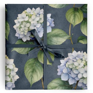 May include: A wrapped gift with a dark blue background and a floral pattern of white and blue hydrangeas and green leaves. A dark blue ribbon is tied around the gift.