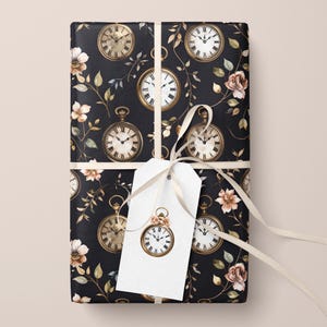 May include: Gift-wrapped package with a black background featuring a repeating pattern of gold-colored pocket watches and floral accents. A white gift tag with a pocket watch design is attached with a cream-colored ribbon.