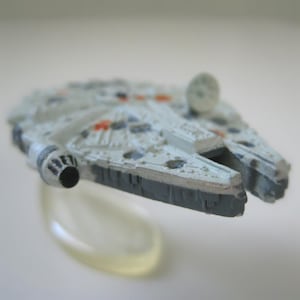 May include: A white and grey toy spaceship with a black engine. The spaceship is on a clear plastic stand.