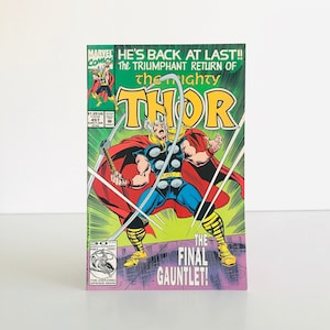 May include: A comic book cover featuring Thor, with the text "HE'S BACK AT LAST!! The Triumphant Return of The Mighty Thor." Thor is depicted with a red cape, blue and yellow attire, and holding a weapon. The cover also includes the text "THE FINAL GAUNTLET!"