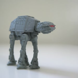 May include: A gray toy model of an AT-AT walker from Star Wars. The walker has four legs and a large body with a cockpit.