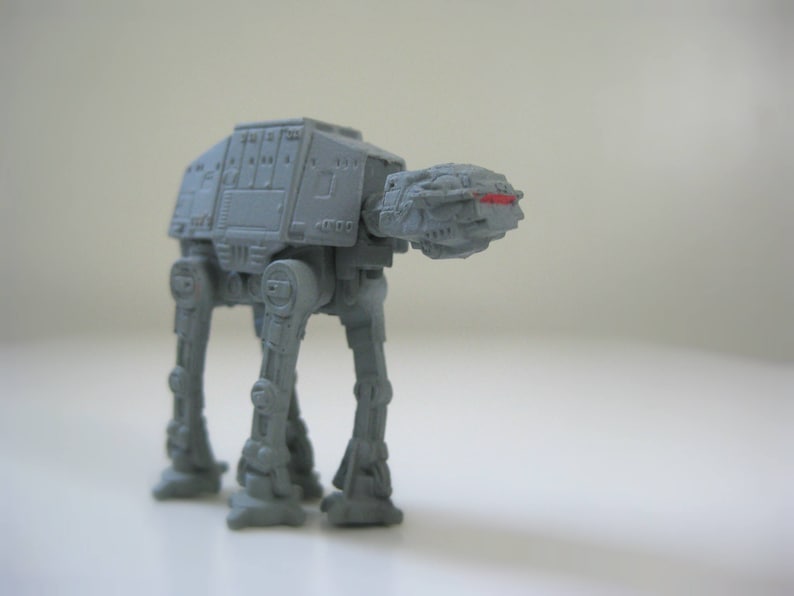 May include: A gray toy model of an AT-AT walker from Star Wars. The walker has four legs and a large body with a cockpit.