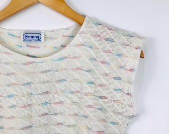 May include: A sleeveless white knit top featuring a diagonal textured pattern with small, multicolored flecks of blue, pink, and yellow throughout. The garment includes a white interior label with the blue text Brunny and Made in U.S.A.