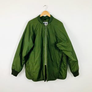 May include: An olive green bomber jacket featuring a full-length front zip, a ribbed collar, and ribbed cuffs. The jacket has a smooth, lightweight outer shell and includes a white interior label with the text R&R Sportswear visible at the neck.