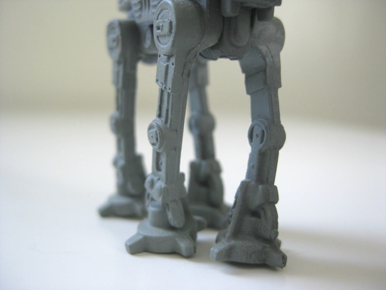 May include: A gray plastic toy robot with articulated legs and feet. The robot has a detailed design with various mechanical parts visible.