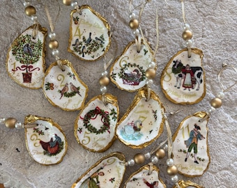 May include: Hand-painted oyster shell Christmas ornaments. Each shell features a gold-painted edge, a unique illustration, and a number from the "Twelve Days of Christmas" carol. The ornaments are strung with gold beads and ribbon.