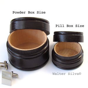 May include: Two wooden boxes, one labeled "Powder Box Size" and the other "Pill Box Size", with lids off, revealing a light wood interior. A pair of silver square cufflinks are in the foreground. The boxes are dark brown.