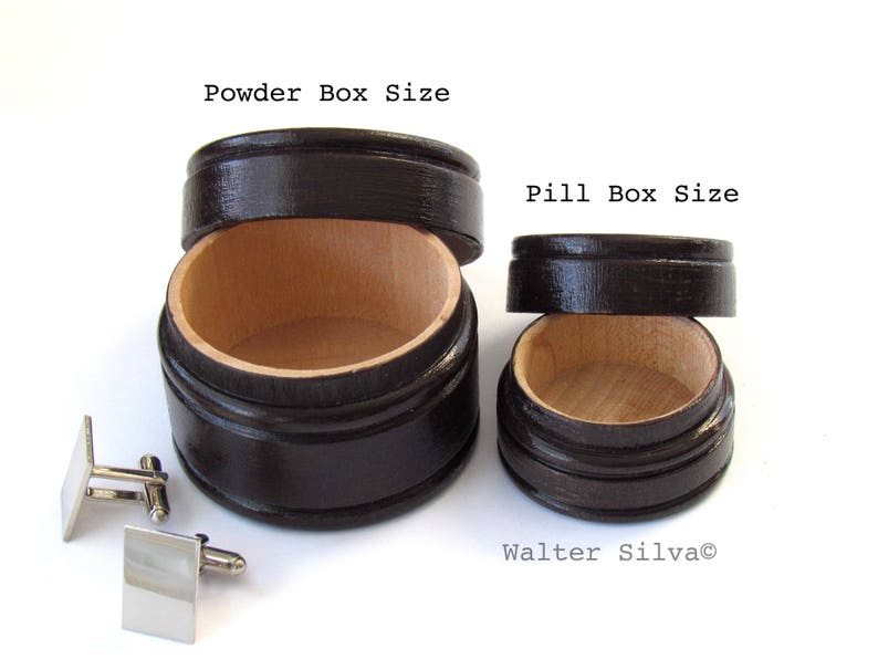 May include: Two wooden boxes, one labeled "Powder Box Size" and the other "Pill Box Size", with lids off, revealing a light wood interior. A pair of silver square cufflinks are in the foreground. The boxes are dark brown.