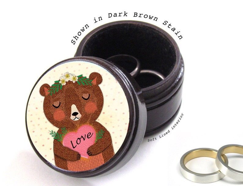 May include: A dark brown wooden ring box with a soft-lined interior. The lid features a cartoon bear holding a pink heart with the word "Love". The box is shown in a dark brown stain.