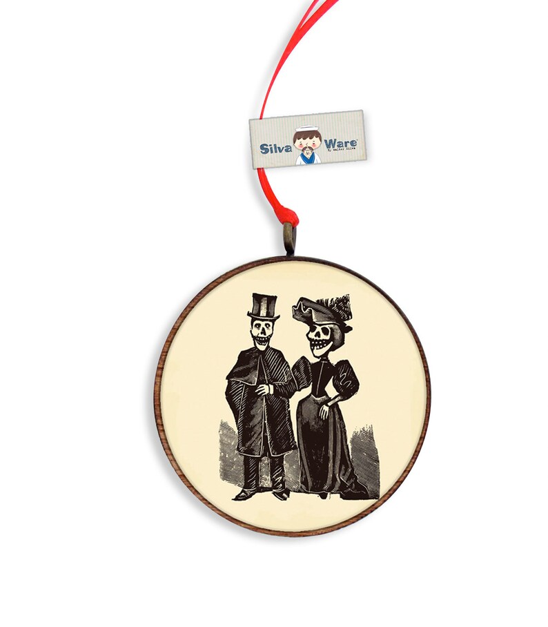 May include: Round wooden ornament featuring a black and white illustration of a skeleton couple in formal attire. The ornament has a light beige background and a dark brown wooden frame. A red ribbon is attached for hanging. The tag reads "Silva Ware".