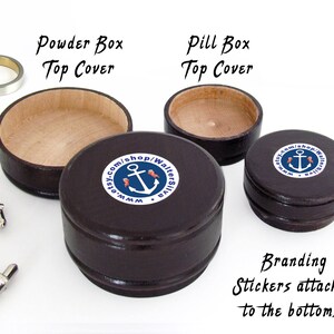 May include: A collection of small, dark brown wooden boxes, including a powder box and pill boxes, with light-colored interiors. The boxes have branding stickers with an anchor logo. Also shown are silver cufflinks and rings.