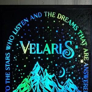 Może przedstawiać: Podświetlany znak w czarnej ramie z g&oacute;rami i rogalem księżyca. Na znaku widnieje napis "To the stars who listen and the dreams that are answered. Velaris."