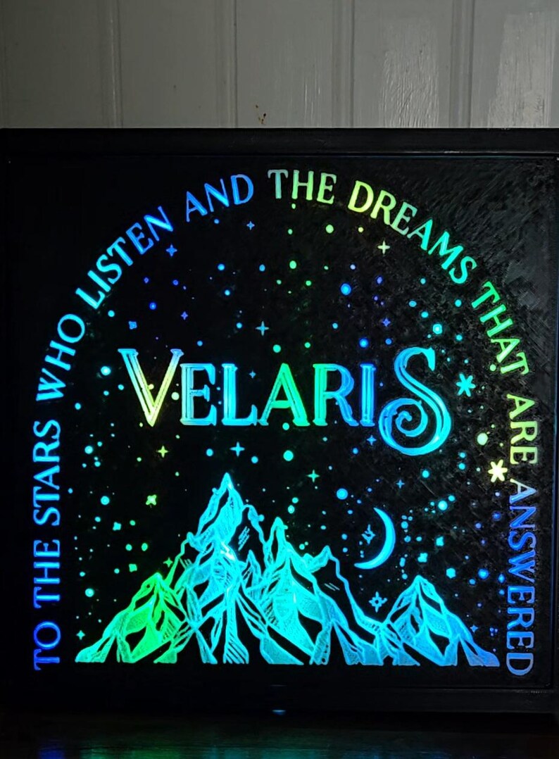 Może przedstawiać: Podświetlany znak w czarnej ramie z g&oacute;rami i rogalem księżyca. Na znaku widnieje napis "To the stars who listen and the dreams that are answered. Velaris."